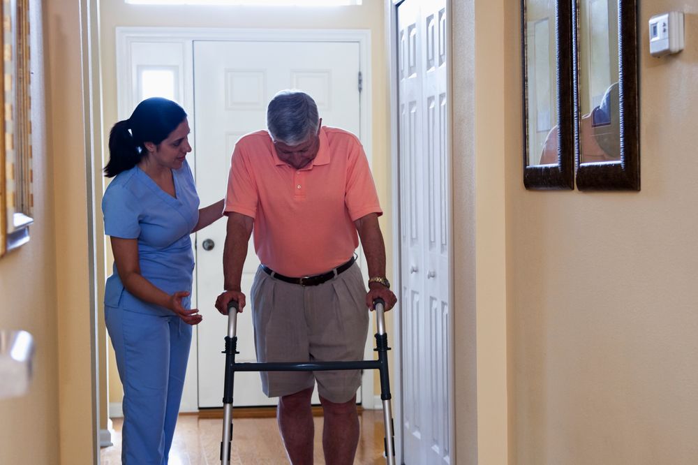 A Jaama caregiver supporting an elderly client with a walker at home