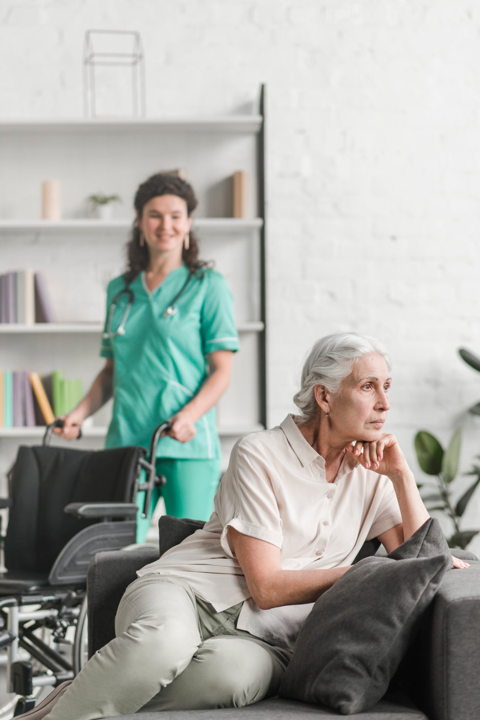 depressed-young-woman-sitting-sofa-front-nurse-standing-with-wheel-chair