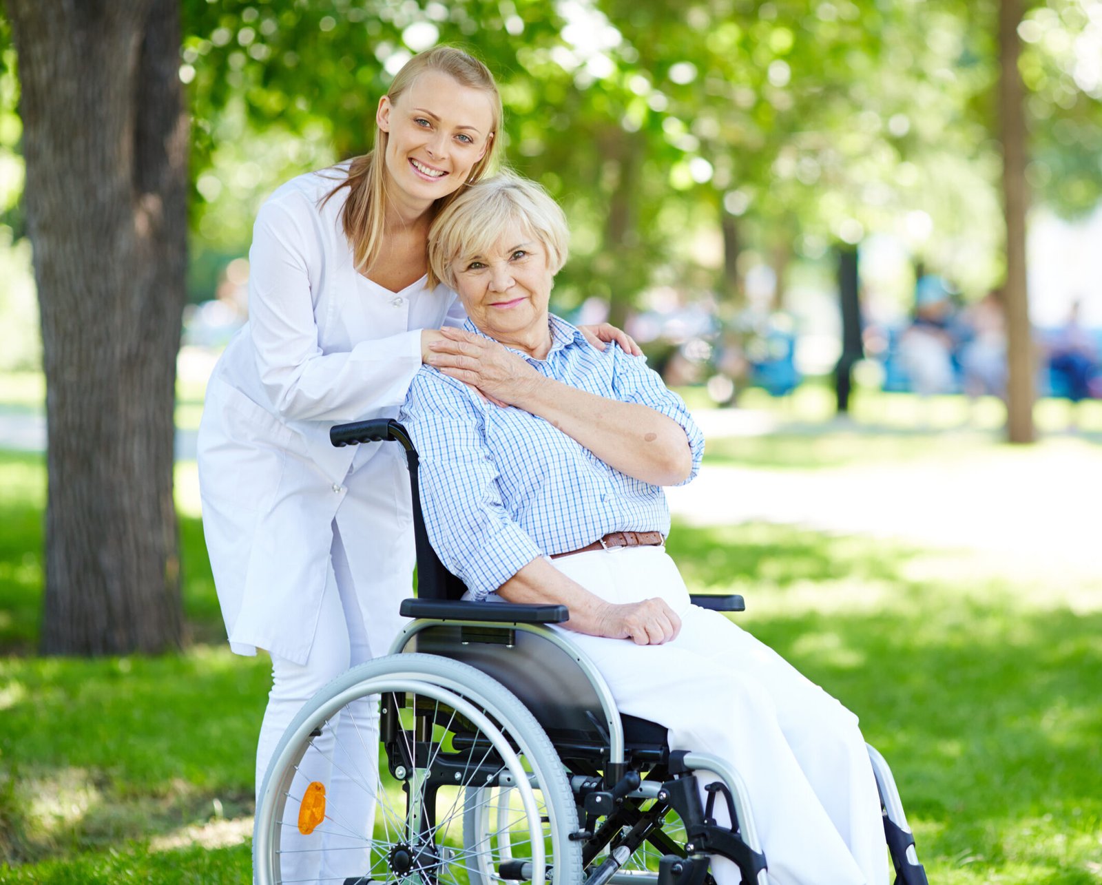 Pretty nurse and senior patient in a wheelchair looking at camera outside